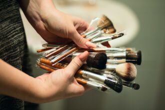 Man is holding a lot of makeup brushes in his hands